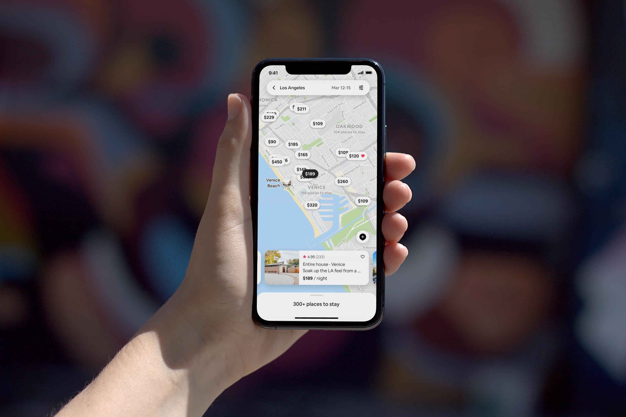 iPhone 11 being held showing an Airbnb search results map view of Los Angeles